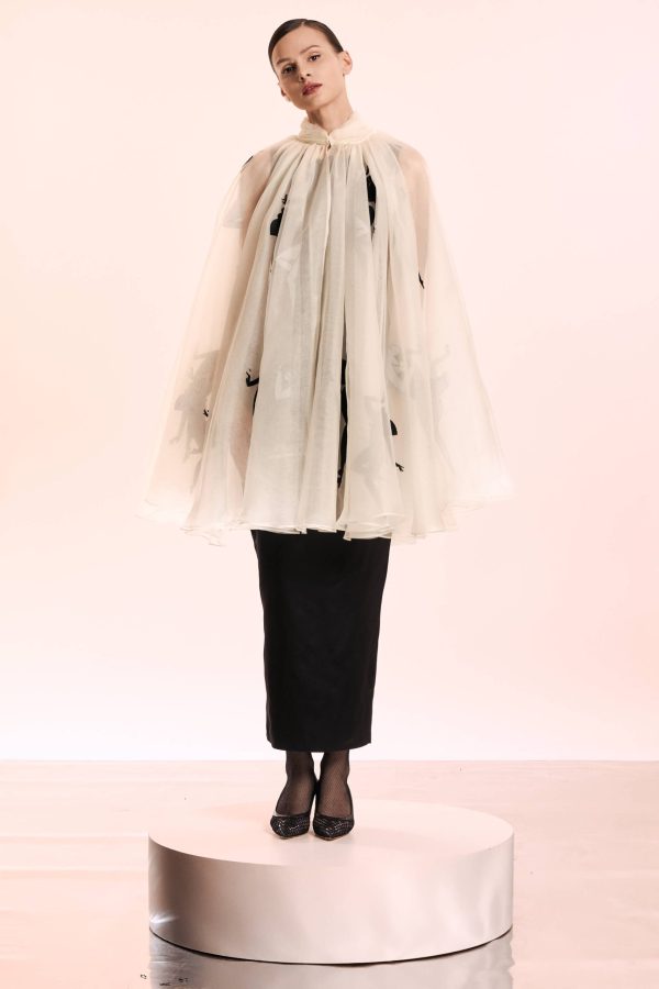 The cape has a breezy shape and it made from natural silk organza. The silhouettes that are embroidered give the product such a glamorous air. The midi black dress made from smooth mikado for a figure-hugging fit and has an elegant slit at the back.