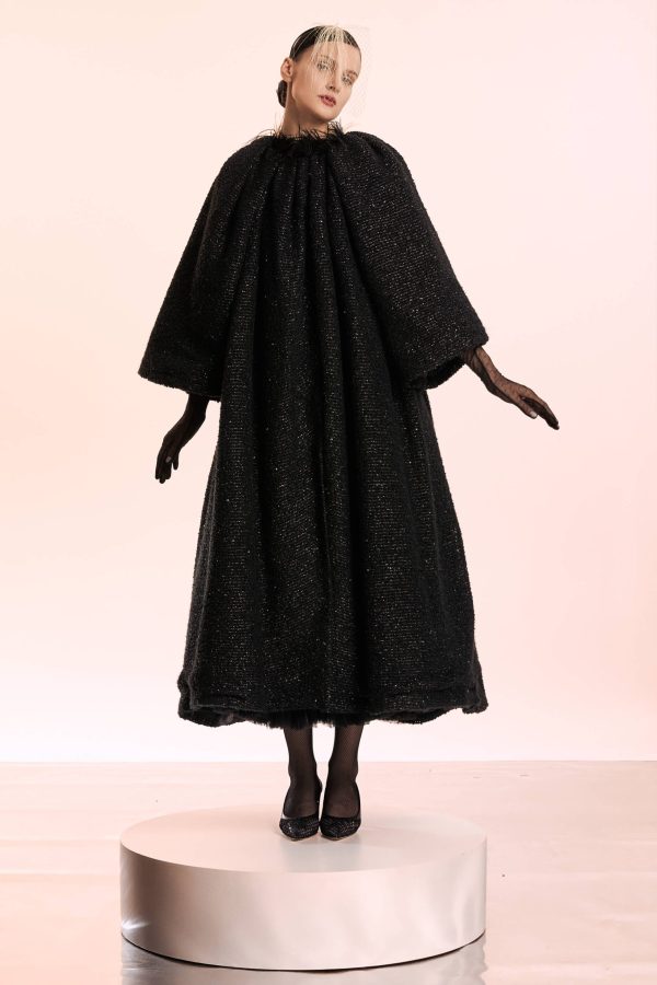 The coat is cut from bucle and has feather finish at the collar. It has vide bell sleeves to create a cape-like effect. On the back it has a hand-made embroidery with a dramatic lily flower in shades of ivory and brick red. It is lined with viscose.