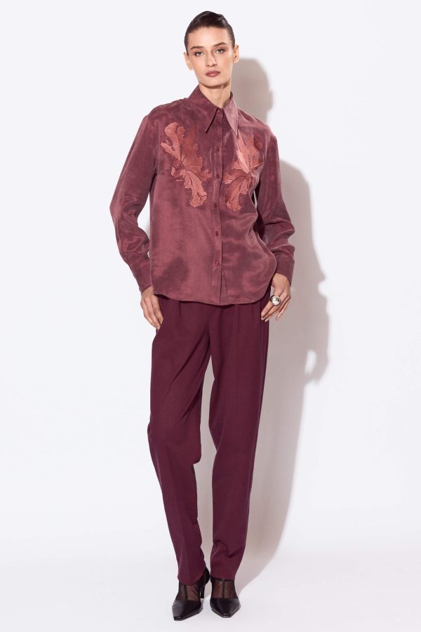 A free volume shirt with a straight silhouette, a curly bottom line, and a length below the hip line. The shoulder line is lowered and it has a symmetrical embroidery on the chest area.