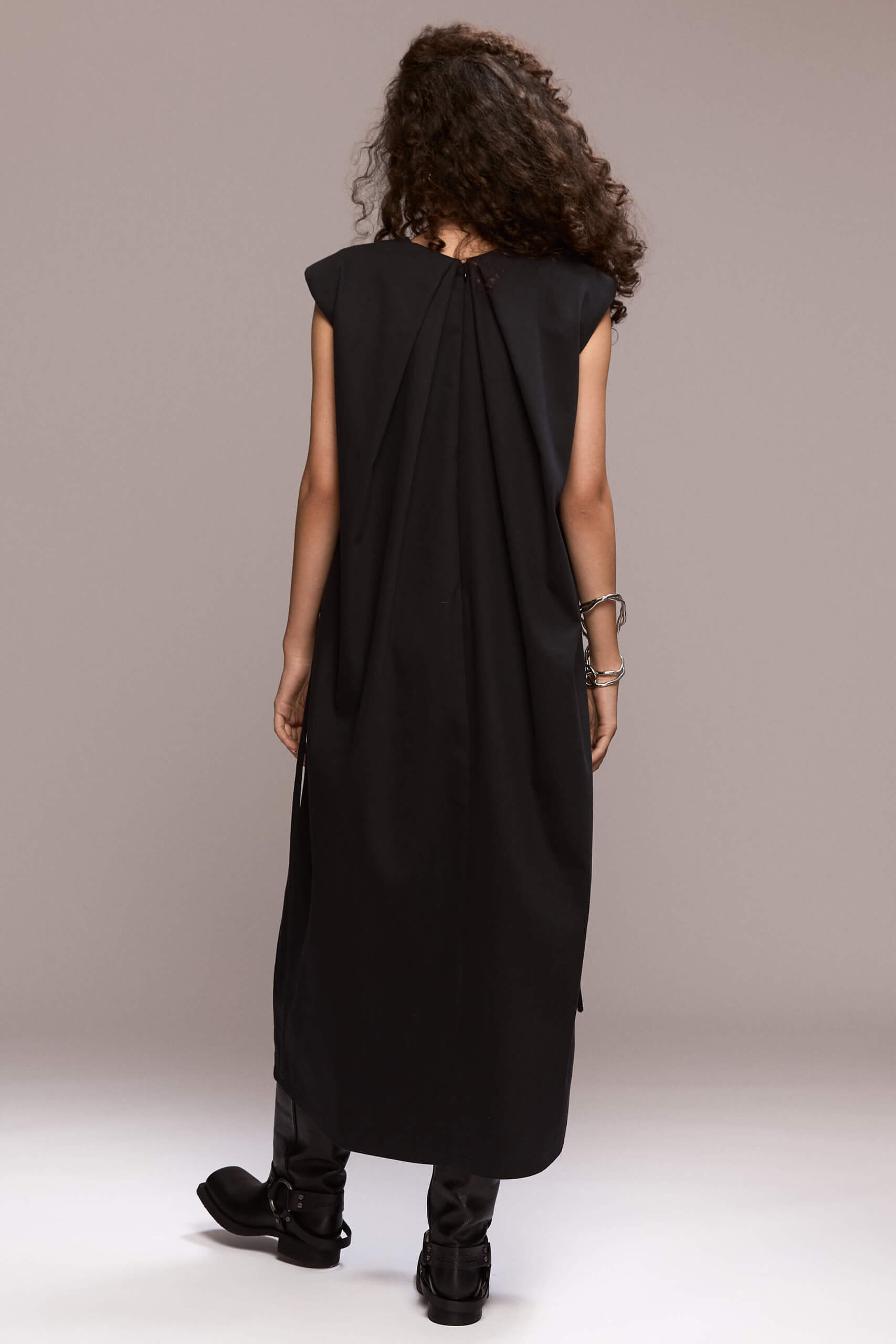 Black sleeveless, loose-fit maxi dress designed to flow on the body, with beautiful back pleats and structured padded shoulders. The dress includes a removable self-tie belt to cinch the waist and side pockets.