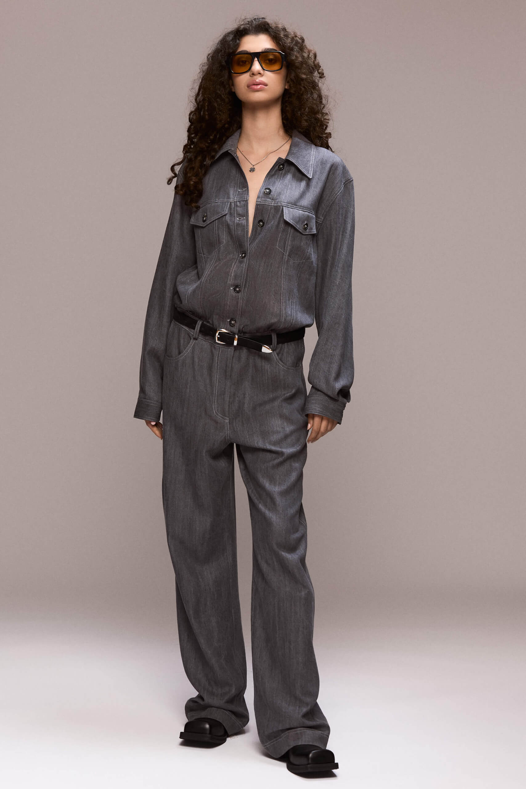 This gray demin boilersuit is a long-sleeved, full-length garment with a straight leg cut, has a front closure with buttons and zipper for the trousers. It features patch pockets on both sides of the chest and 4 functional ones, two in front and other two on the back of the trousers. Its fit is comfortable yet flattering, making it a versatile wardrobe piece. Wear it on it's own or with a contrasting belt.