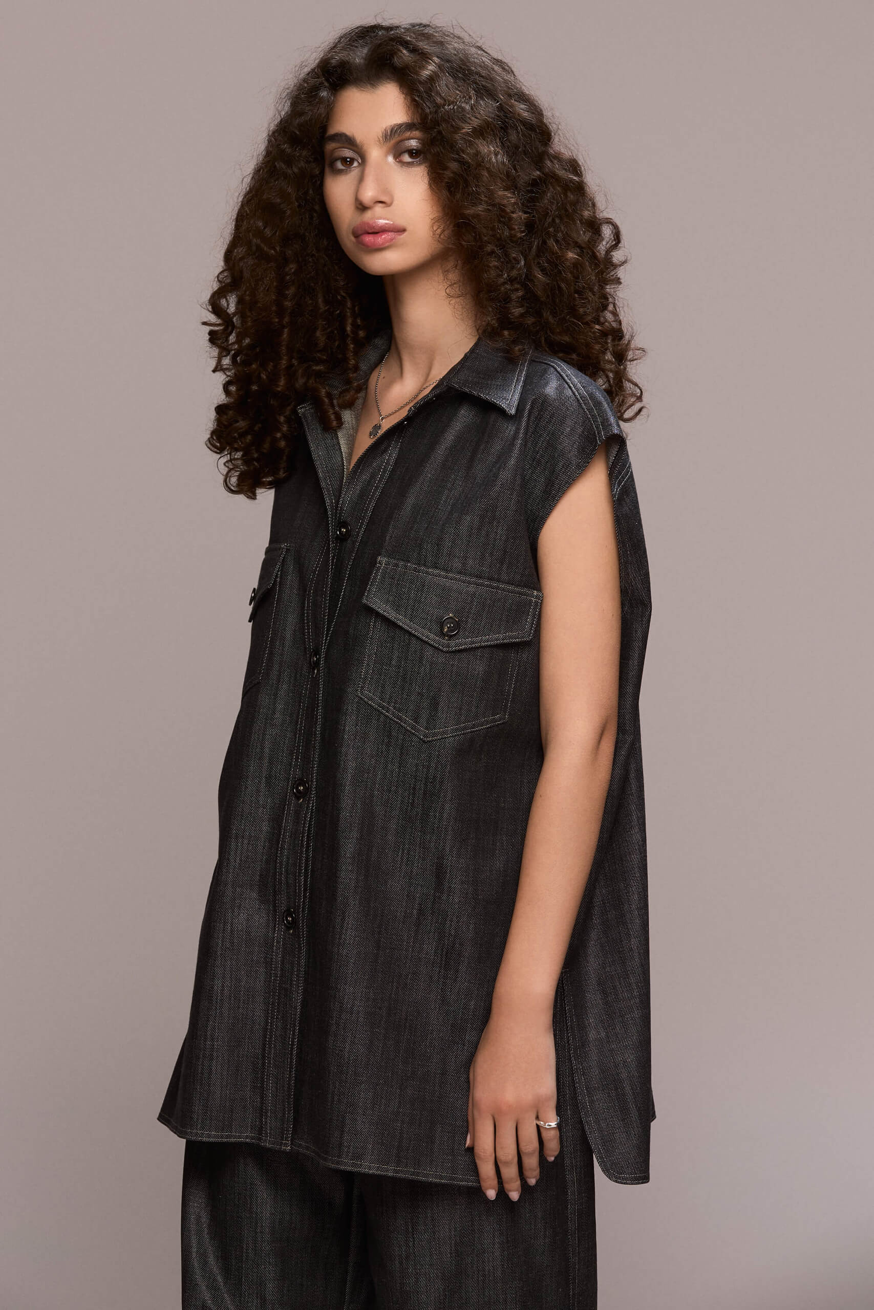 A sleveless, oversized button-down shirt featuring a collared neckline and dual chest pockets, this piece gives a distinctly modern and eye-catching appearance. Wear it with our matching wide leg trousers for a full statement look.