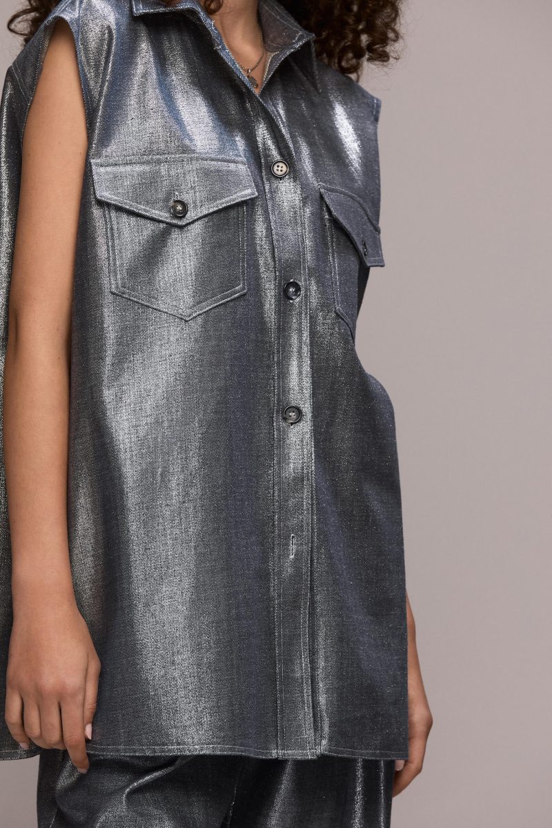 A sleveless, oversized button-down shirt featuring a collared neckline and dual chest pockets, this piece gives a distinctly modern and eye-catching appearance. Wear it with our matching wide leg trousers for a full statement look.