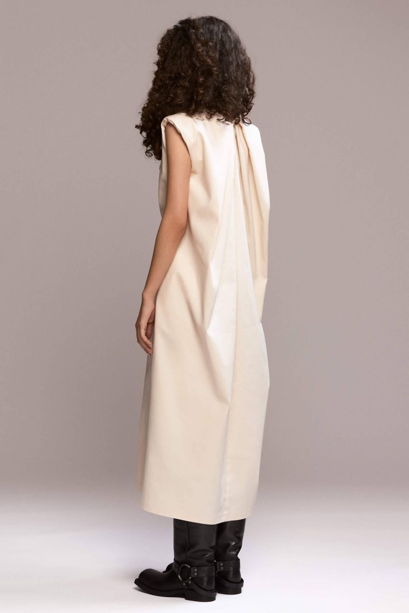 Off-white sleeveless, loose-fit maxi dress designed to flow on the body, with beautiful back pleats and structured padded shoulders. The dress includes a removable self-tie belt to cinch the waist and side pockets.