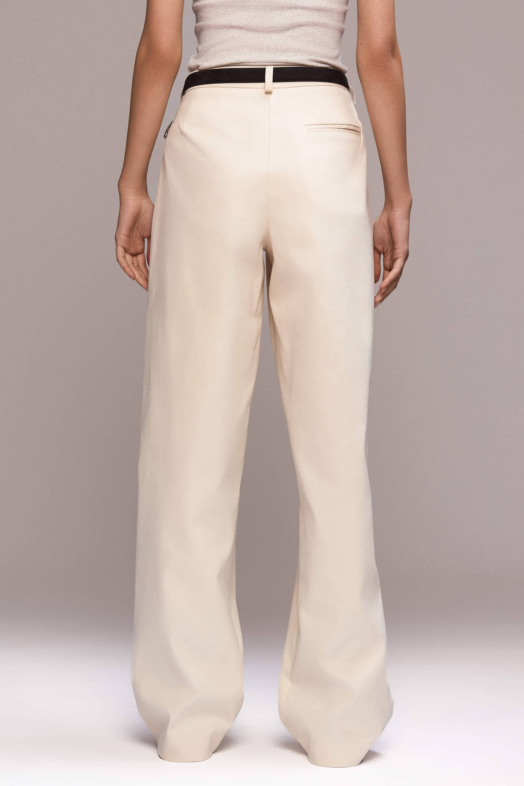 These wide-leg ivory trousers feature front pleats, which give them a relaxed silhouette. They have full length, front pockets and one single back pocket on the right side. There is a fly front zipper closure.