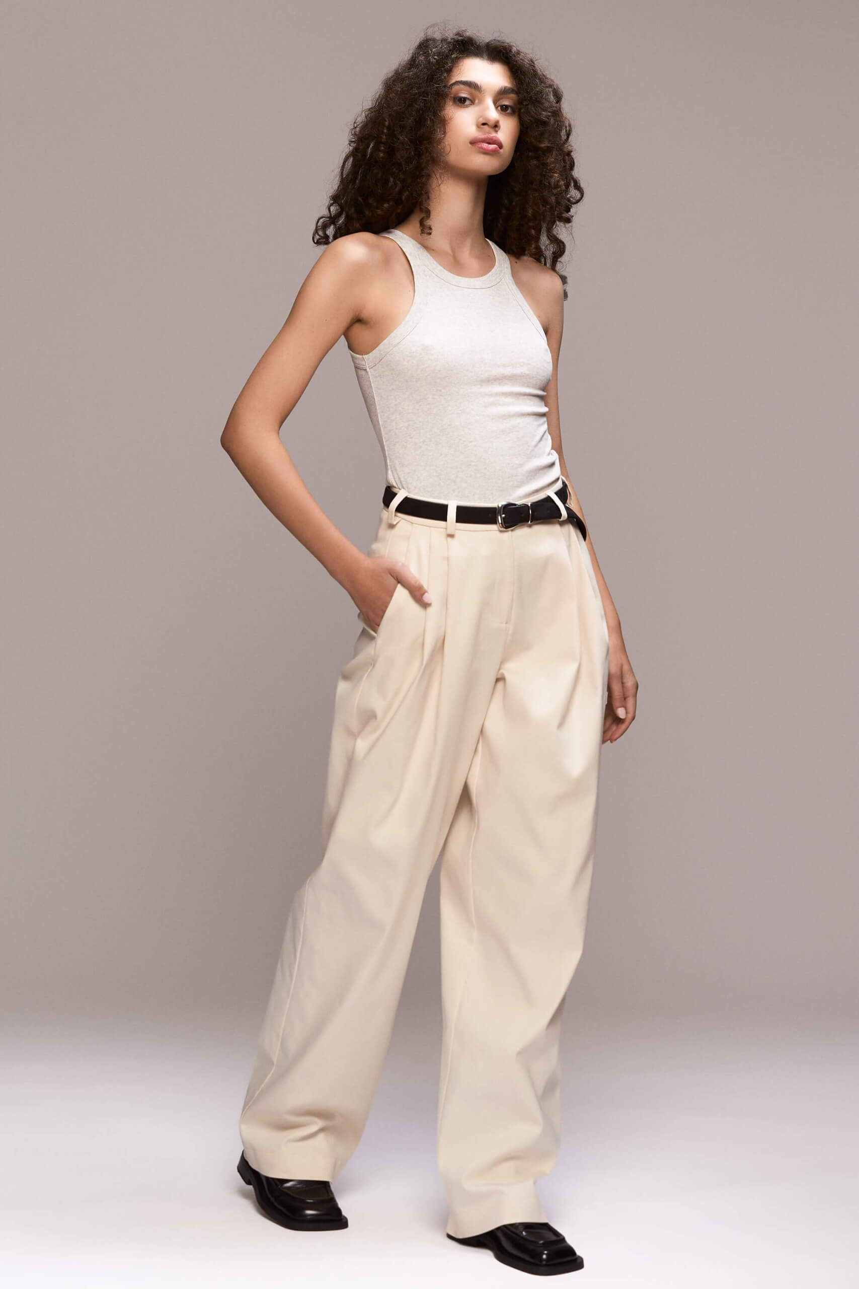 These wide-leg ivory trousers feature front pleats, which give them a relaxed silhouette. They have full length, front pockets and one single back pocket on the right side. There is a fly front zipper closure.