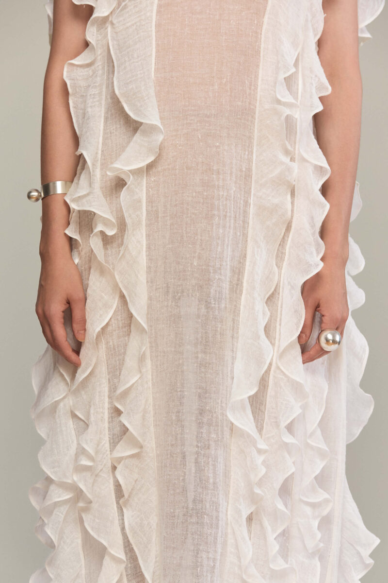 The frilled maxi dress has a loose fit, with a sleeveless design and a round neckline. It features layered ruffles on both the front and back giving it a fluid and feminine look. It is the perfect choice for summer events, or a bohemian-inspired look.