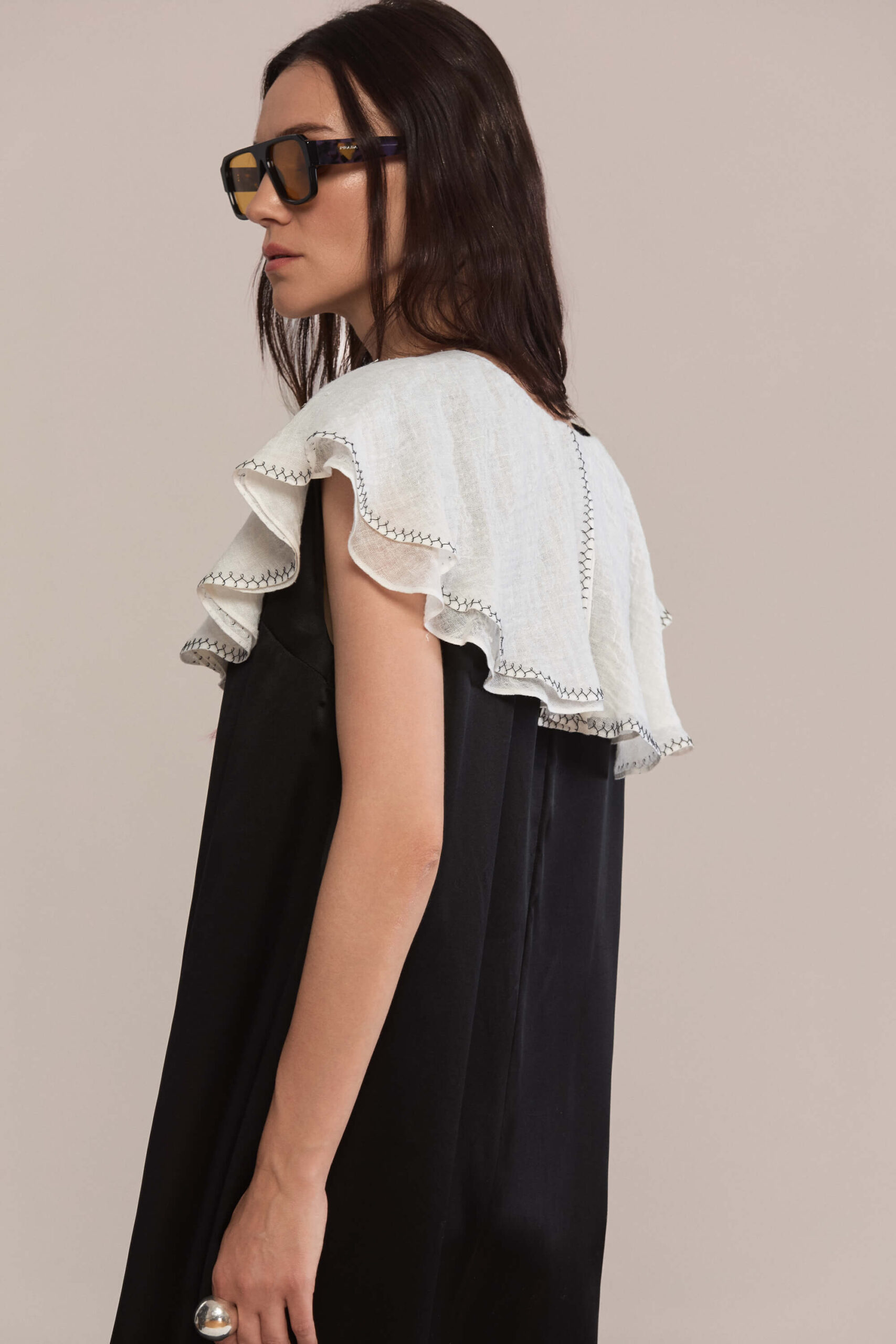 A floor-length black silk dress with a sleek, straight silhouette. The dramatic oversized white ruffled linen collar falls elegantly over the shoulders, offering a bold contrast and refined monochrome appeal. This dress is a true statement.