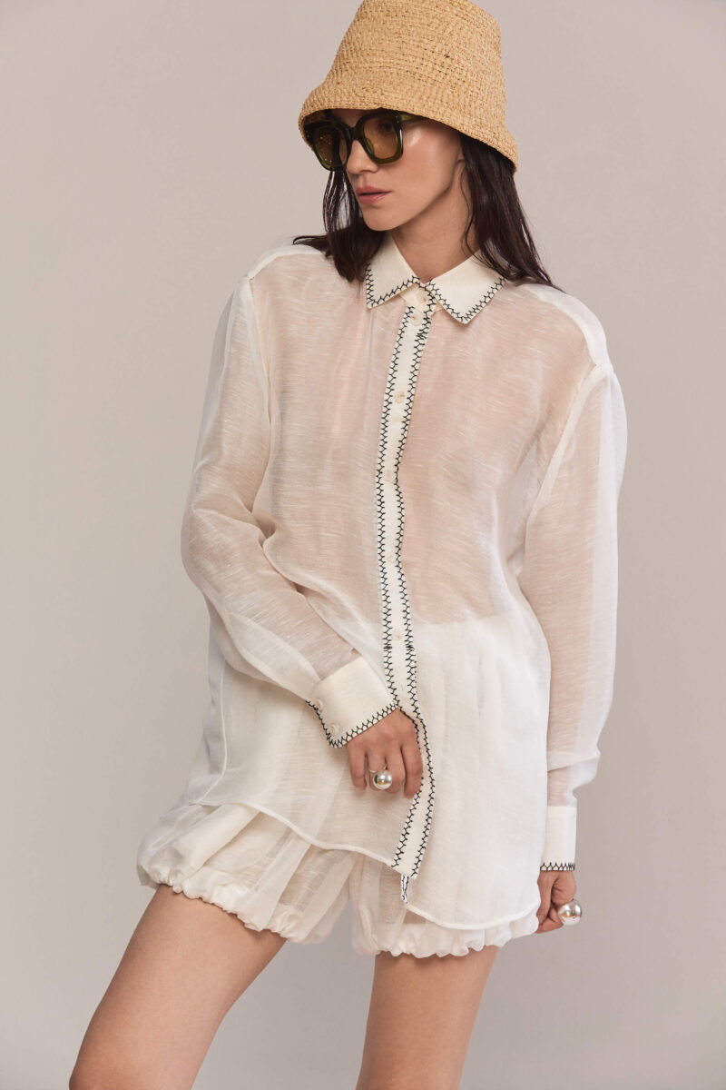 This oversized, semi-sheer shirt features a relaxed fit with long sleeves and a classic pointed collar. Black contrast hand stitch embroidery highlights the collar, front placket, and cuffs, creating a subtle, handcrafted minimalist aesthetic. Wear them with our classic black trousers for a total look.